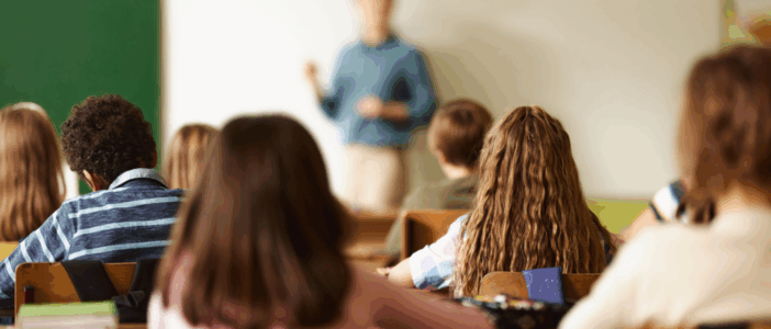 School classroom with children looking at a teacher in the background